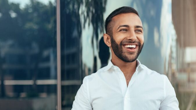 Portrait Of A Young Confident Smiling Indian Man Holding A Tablet And Looking Into The Distance