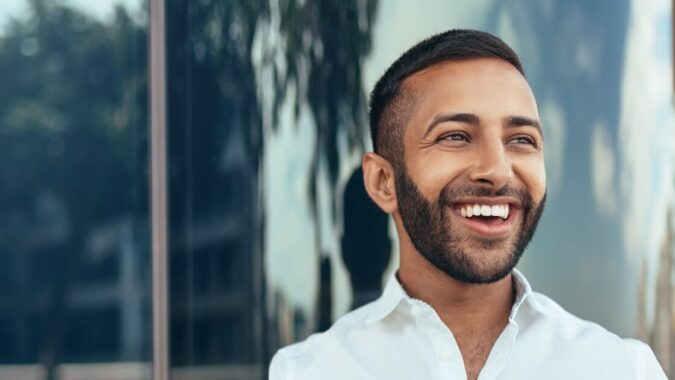 Portrait Of A Young Confident Smiling Indian Man Holding A Tablet And Looking Into The Distance