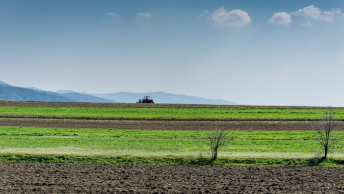 Ackerlandschaft mit Bergen im Hintergrund und einem Tracktor in der Ferne