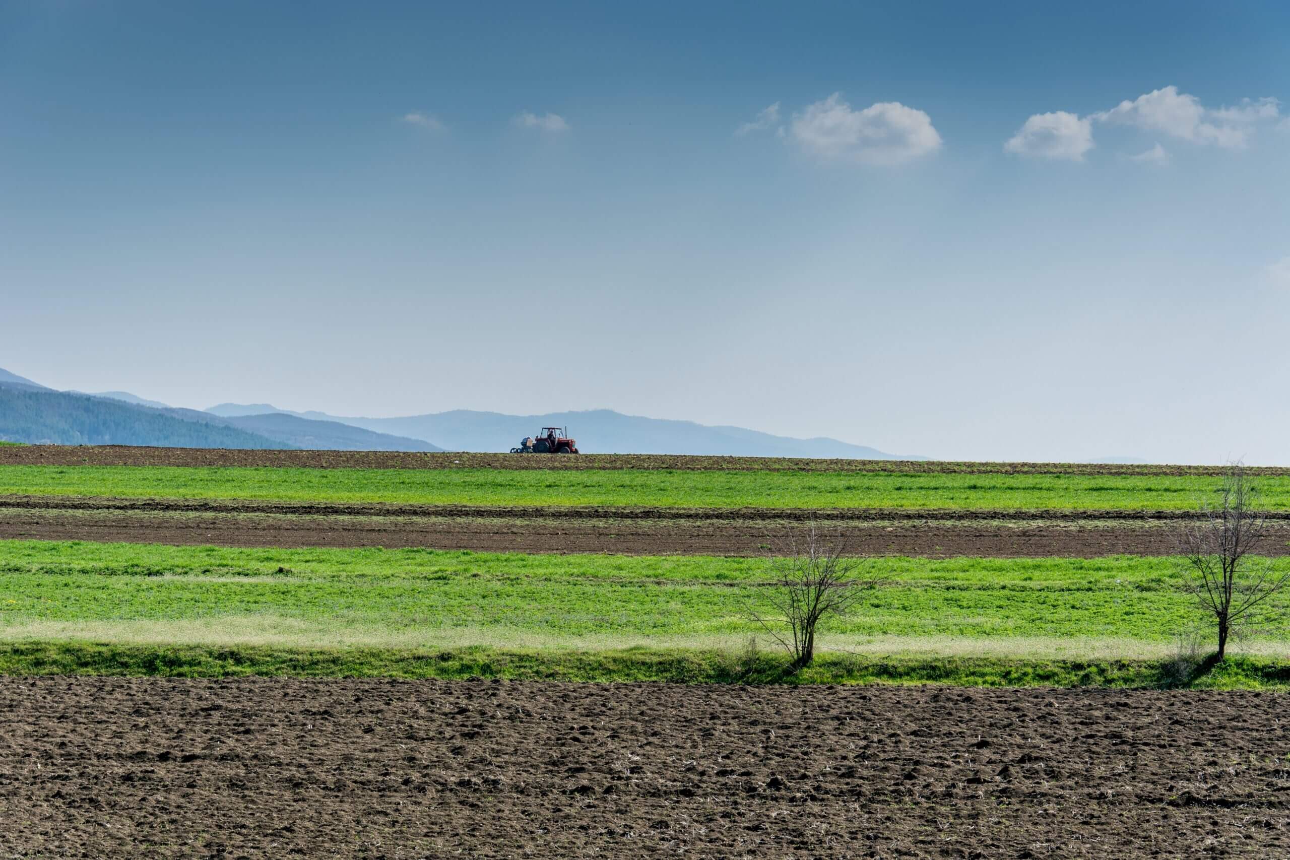 Ackerlandschaft mit Bergen im Hintergrund und einem Tracktor in der Ferne