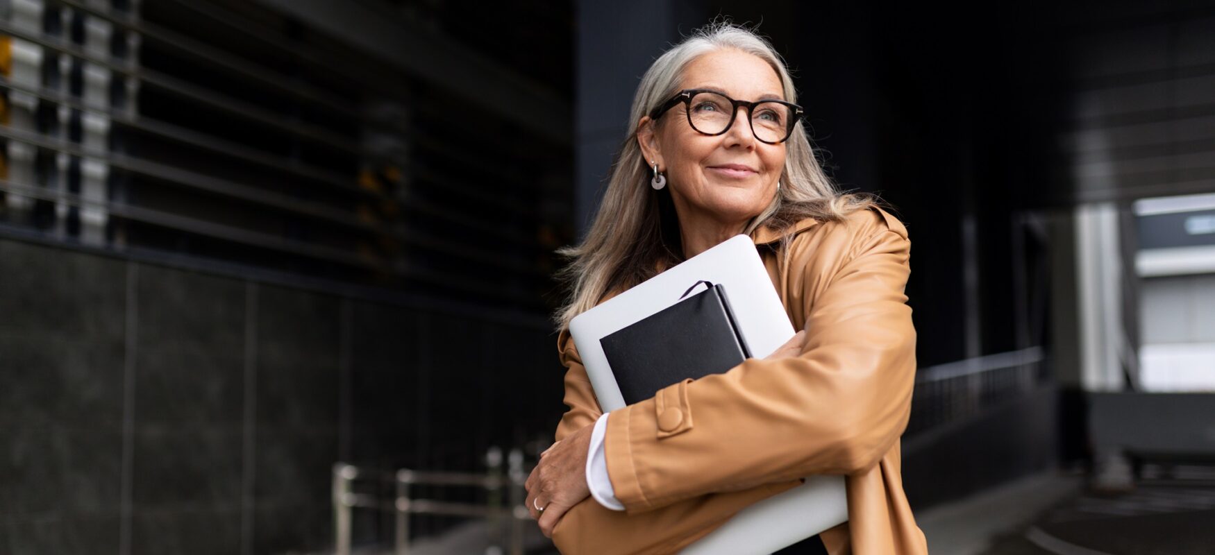 Portrait of an elderly businesswoman with a laptop in glasses outside the office.